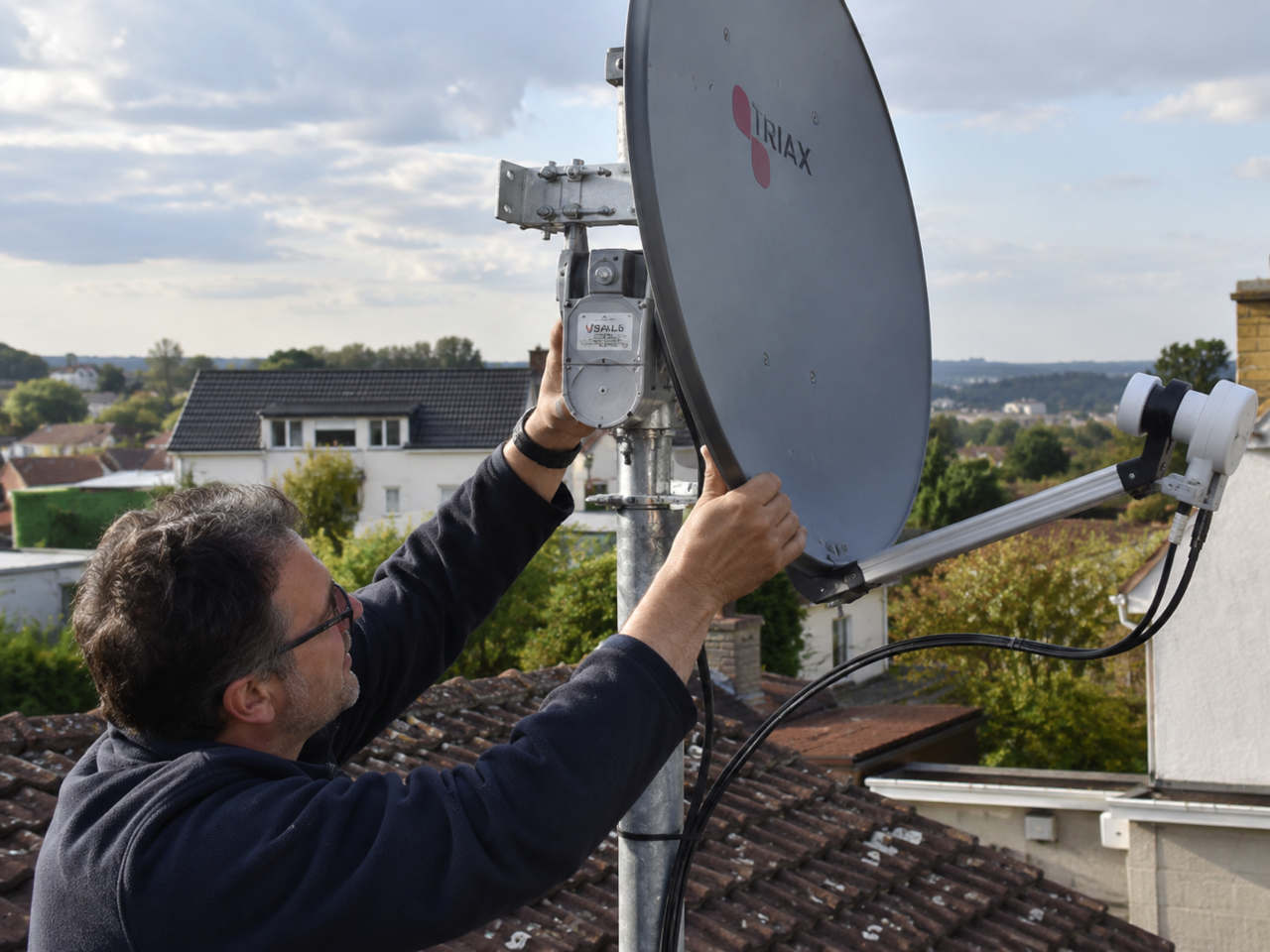 Man adjusting a motorized satellite dish with a USALS motor on a residential rooftop.