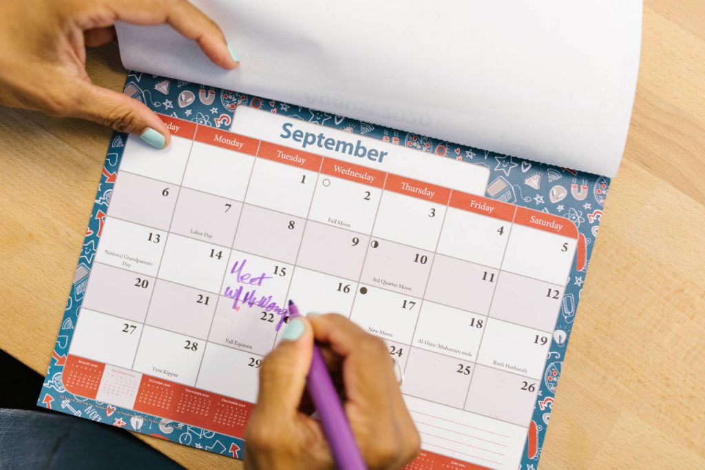 Close-up of a person writing an appointment on a September paper calendar with a purple pen.