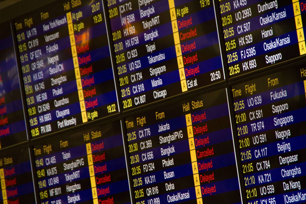 Airport flight information boards showing numerous delayed and cancelled flights, highlighting travel disruptions and schedule changes.