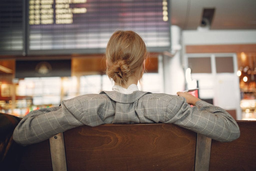Woman sitting in an airport terminal, looking toward a flight information board while waiting for her flight.