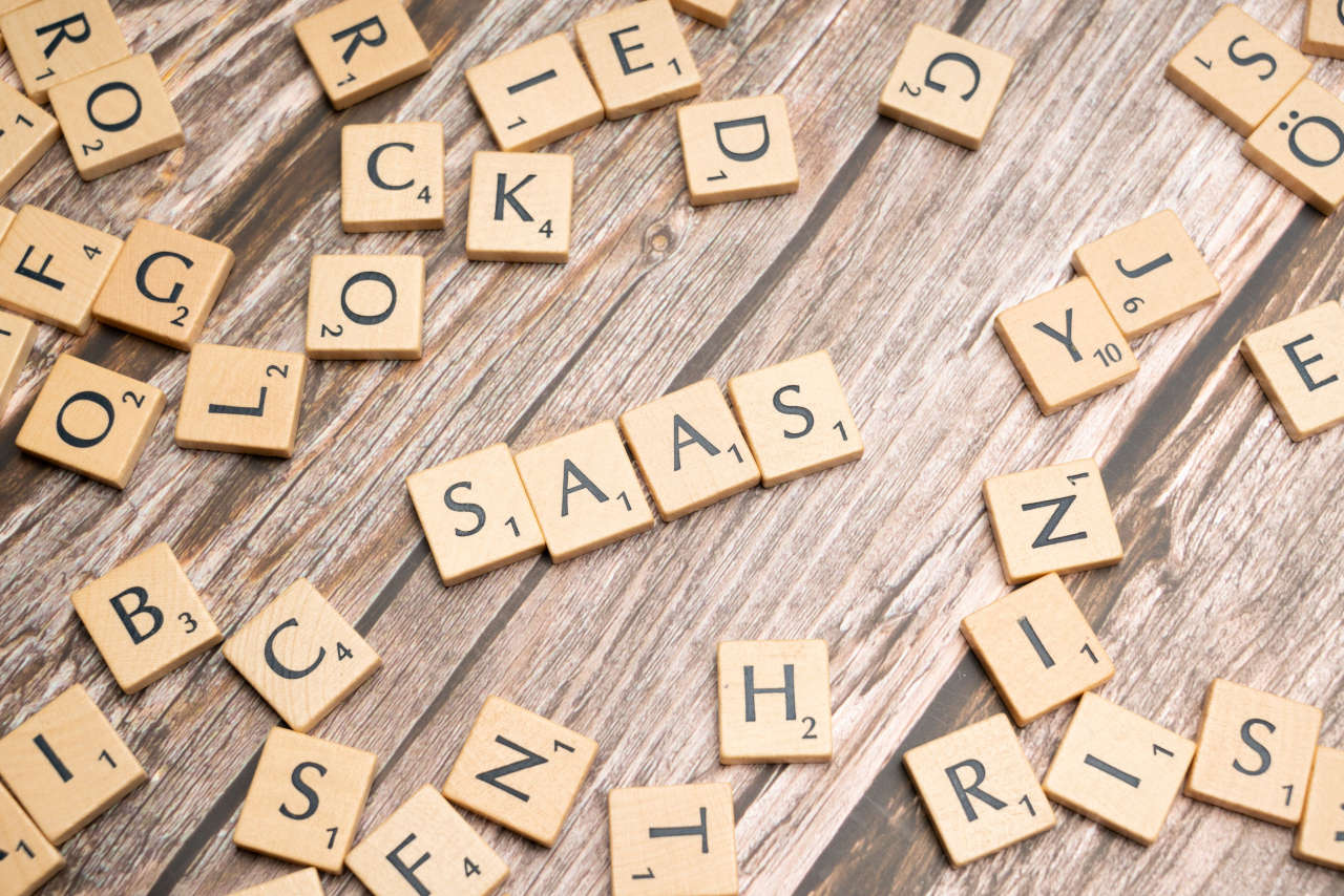 Wooden letter tiles spelling “SAAS” surrounded by scattered alphabet tiles on a rustic wooden surface.