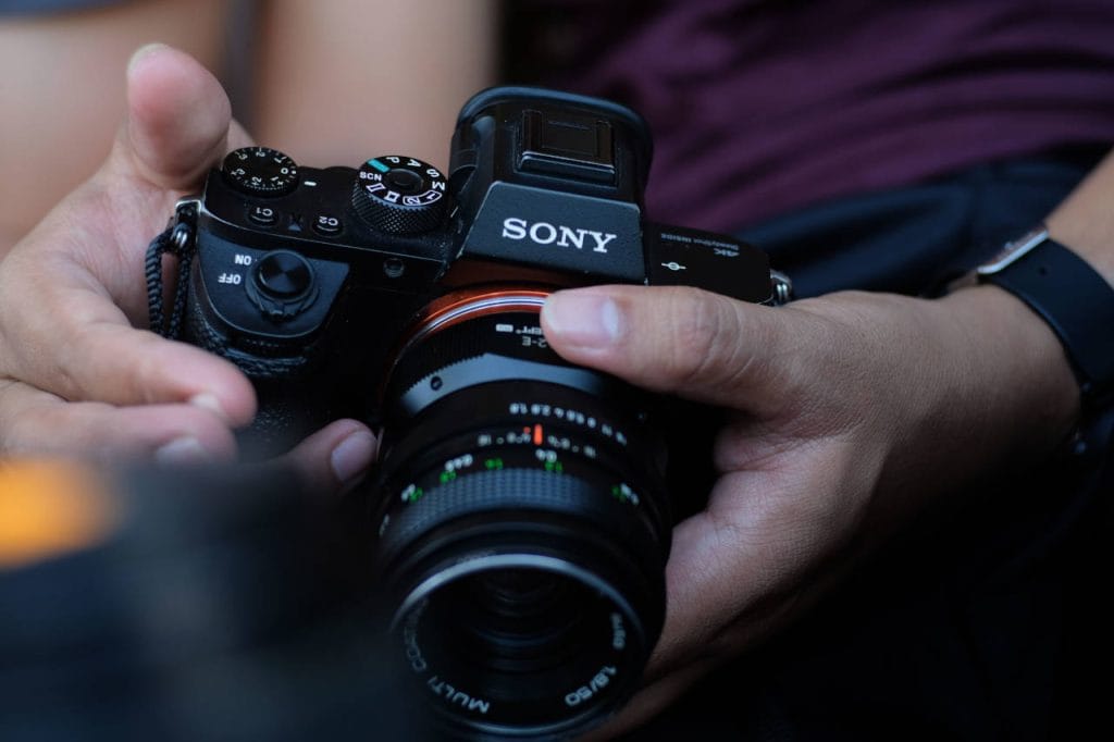 Close-up of a Sony Alpha mirrorless camera with a manual-focus lens, held in a photographer’s hands.