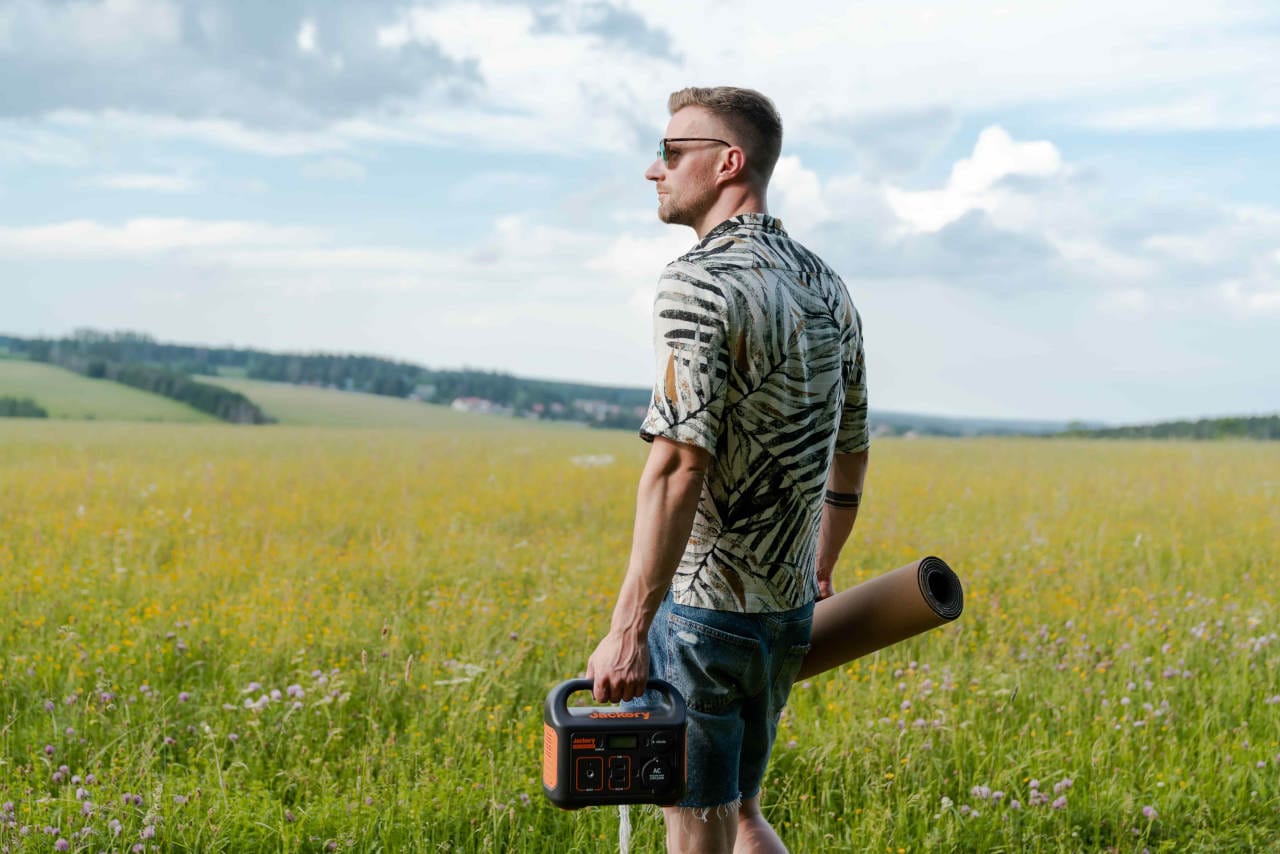 Man carrying a Jackery portable power station across a field with camping gear